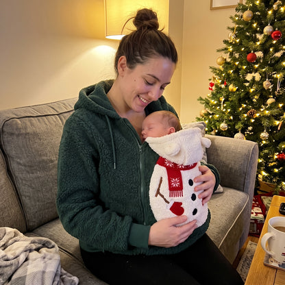 Young mum in the Mistletot Snowman baby pouch hoodie on the sofa by the Christmas tree, her baby asleep chest to chest